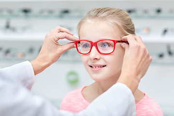 Image showing optician putting glasses to girl at optics store