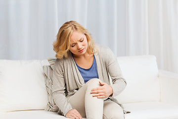 Image showing unhappy woman suffering from pain in leg at home