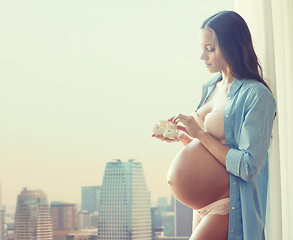 Image showing happy pregnant woman with baby booties at home