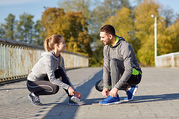 Image showing smiling couple tying shoelaces outdoors