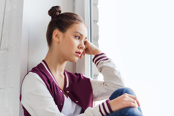 Image showing sad pretty teenage girl sitting on windowsill