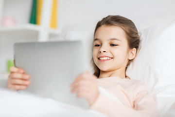 Image showing happy girl lying in bed with tablet pc at home