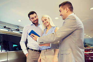 Image showing happy couple with car dealer in auto show or salon