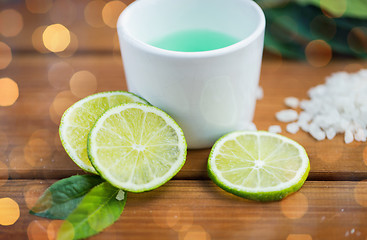 Image showing close up of body lotion in cup and limes on wood