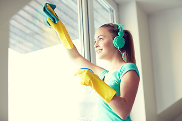 Image showing happy woman with headphones cleaning window