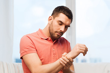 Image showing unhappy man suffering from pain in hand at home