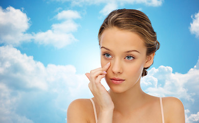 Image showing young woman applying cream to face over blue sky