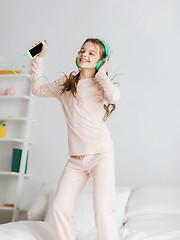 Image showing girl jumping on bed with smartphone and headphones