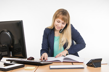 Image showing Business woman talking on the phone, looking for the right information at the office book