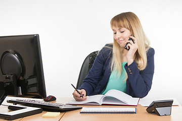 Image showing Business woman talking on the phone and writes in the book office