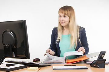 Image showing Office Specialist leafing through paper documents folder looked into the computer