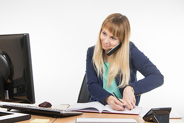 Image showing Business woman talking on the phone, record information in the office book and looked at the monitor
