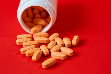 Image showing Pills spilling out of pill bottle on red. Top view with copy space. 