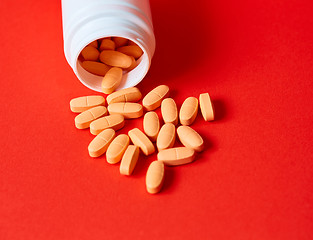 Image showing Pills spilling out of pill bottle on red. Top view with copy space. 