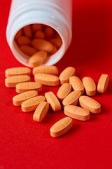 Image showing Pills spilling out of pill bottle on red. Top view with copy space. 