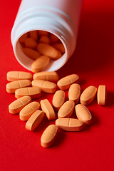 Image showing Pills spilling out of pill bottle on red. Top view with copy space. 