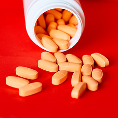 Image showing Pills spilling out of pill bottle on red. Top view with copy space. 