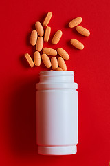 Image showing Pills spilling out of pill bottle on red. Top view with copy space. 