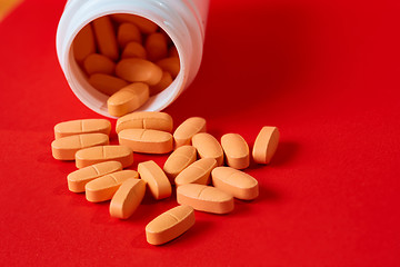 Image showing Pills spilling out of pill bottle on red. Top view with copy space. 