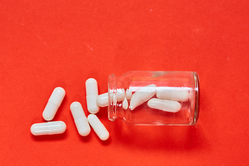 Image showing Pills spilling out of pill bottle on red. Top view with copy space. 