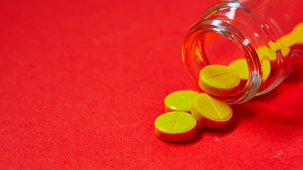 Image showing Pills spilling out of pill bottle on red. Top view with copy space. 