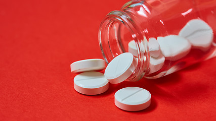 Image showing Pills spilling out of pill bottle on red. Top view with copy space. 