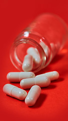 Image showing Pills spilling out of pill bottle on red. Top view with copy space. 