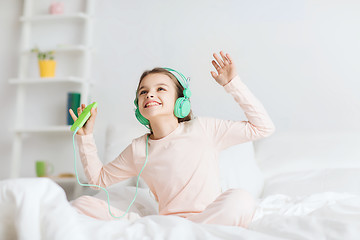 Image showing girl sitting on bed with smartphone and headphones