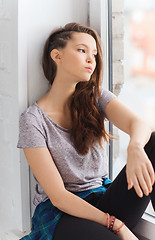 Image showing sad pretty teenage girl sitting on windowsill