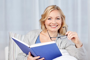 Image showing smiling woman reading book and sitting on couch