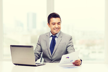 Image showing smiling businessman with laptop and papers