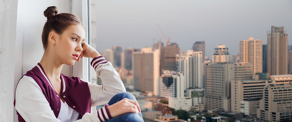 Image showing sad pretty teenage girl sitting on windowsill