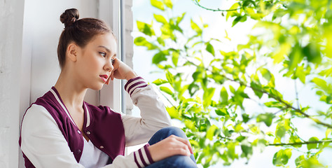 Image showing sad pretty teenage girl sitting on windowsill