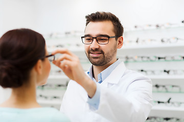 Image showing optician putting glasses to woman at optics store