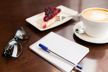 Image showing close up of notebook with pen, coffee cup and cake