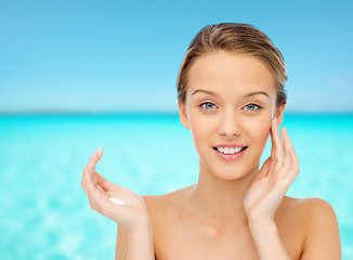 Image showing happy young woman applying cream to her face