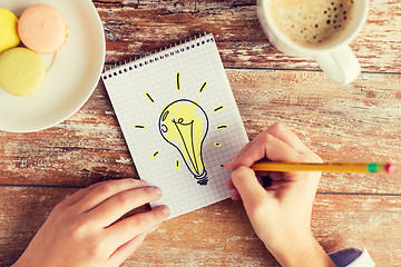 Image showing close up of hands drawing bulb to notebook