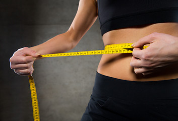 Image showing close up of woman measuring waist by tape in gym