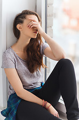 Image showing sad pretty teenage girl sitting on windowsill