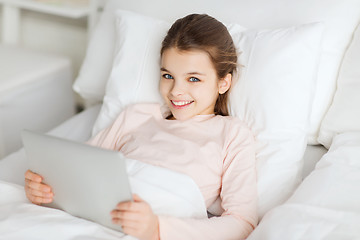 Image showing happy girl lying in bed with tablet pc at home