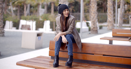 Image showing Fashionable young woman sitting waiting on a bench