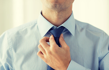 Image showing close up of man in shirt adjusting tie on neck