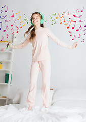 Image showing girl jumping on bed with smartphone and headphones