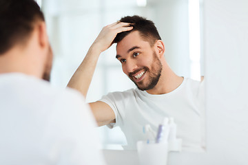 Image showing happy young man looking to mirror at home bathroom