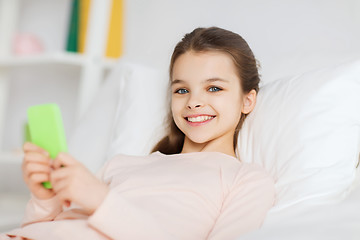 Image showing happy girl lying in bed with smartphone at home