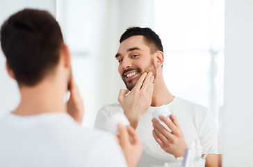 Image showing happy young man applying cream to face at bathroom