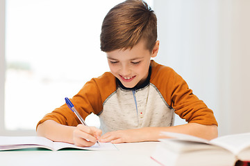 Image showing smiling student boy writing to notebook at home