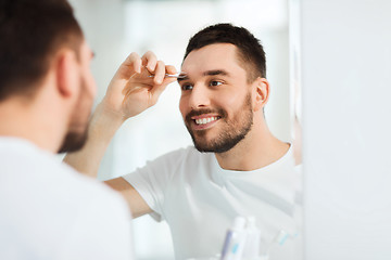 Image showing man with tweezers tweezing eyebrow at bathroom