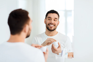 Image showing happy young man applying cream to face at bathroom