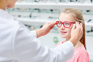 Image showing optician putting glasses to girl at optics store